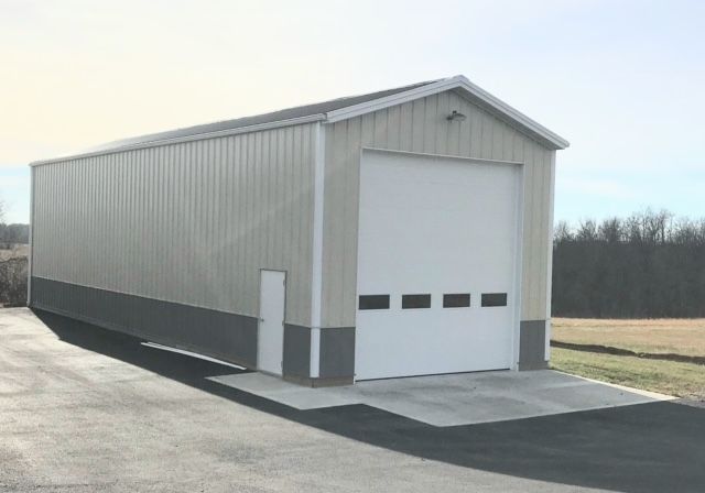 A large metal building with a white garage door is sitting on the side of a road.