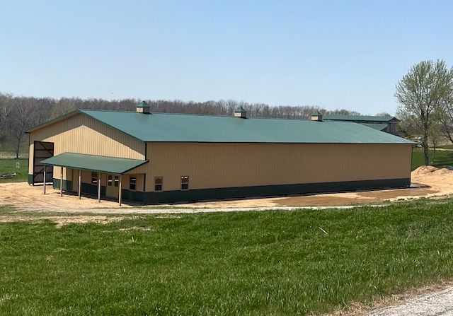 A large building with a green roof is sitting in the middle of a grassy field.