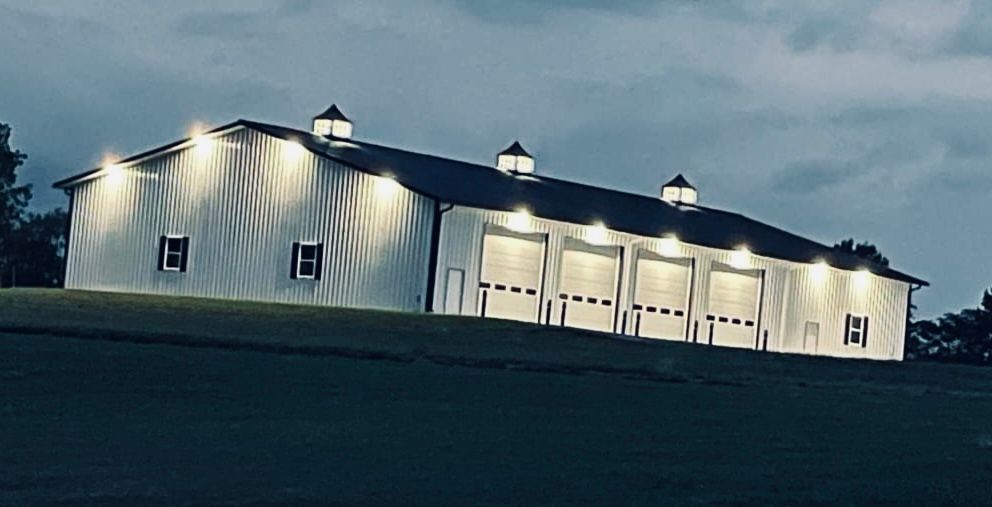 A large white barn is lit up at night on top of a hill.