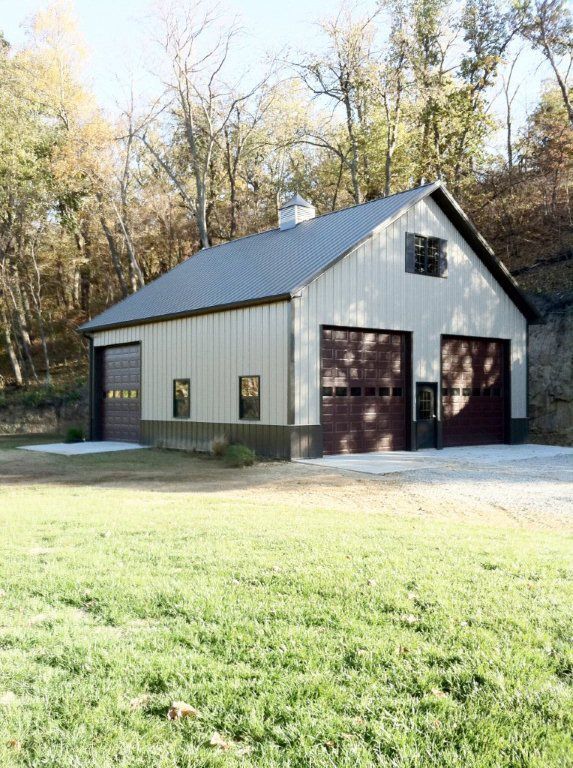 A garage with two garage doors is sitting in the middle of a grassy field.